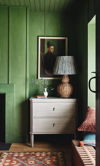 green living room, with matching painted ceiling, lime wash chest of drawers, art work, large lamp, rug, wooden floor, radiator