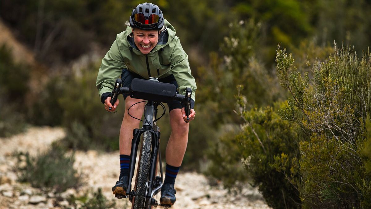 A happy woman riding a gravel bike on a rocky trail