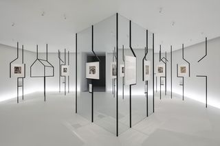 White room with artworks displayed using black strips from the ceiling and floor