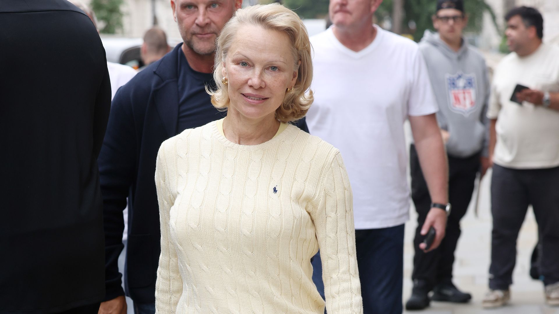 Pamela Anderson walks outside in London wears a yellow knit and yellow maxi skirt with white and gold trainers.