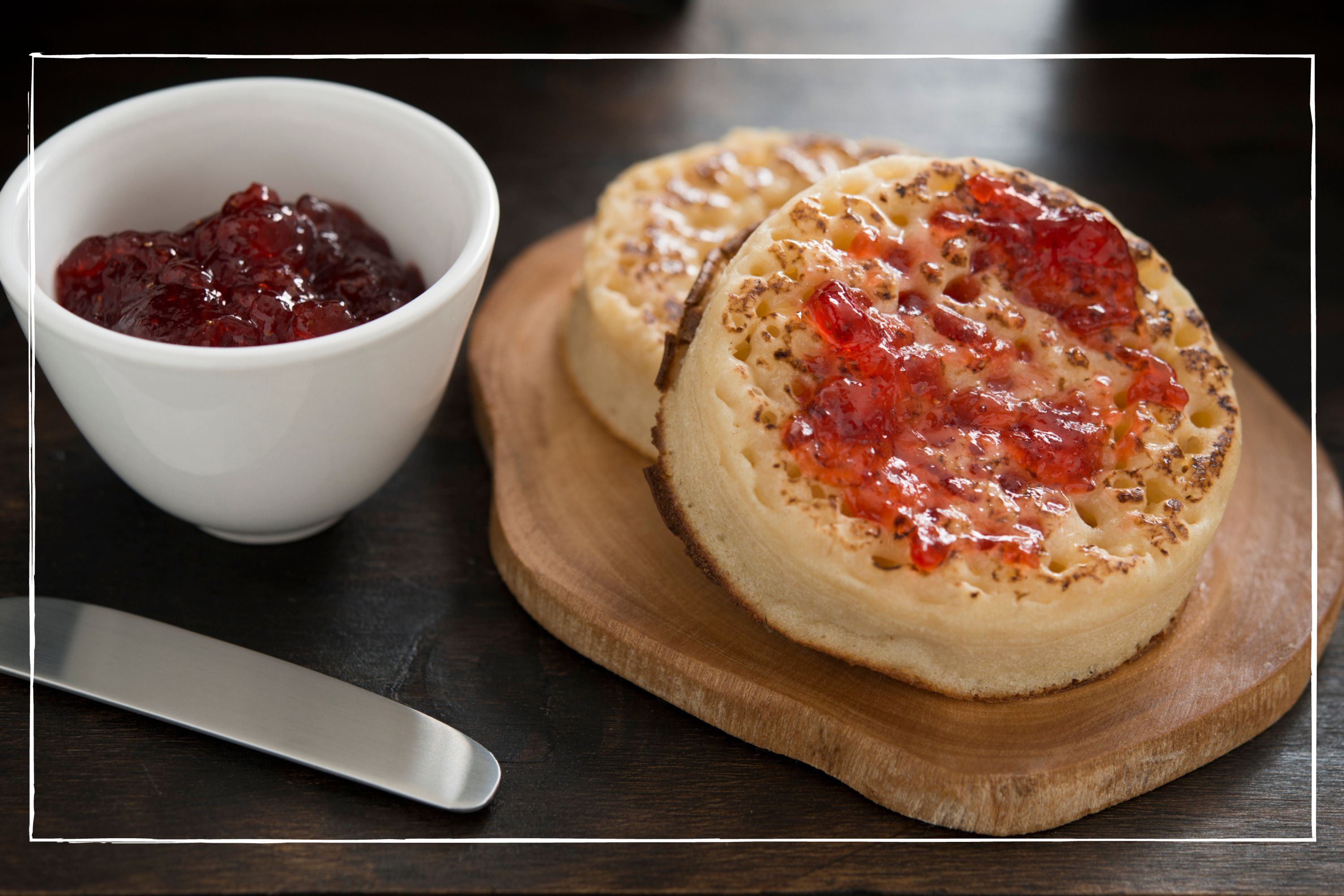 Toasted crumpets with jam, arranged artfully on a wooden board next to a pot of strawberry jam
