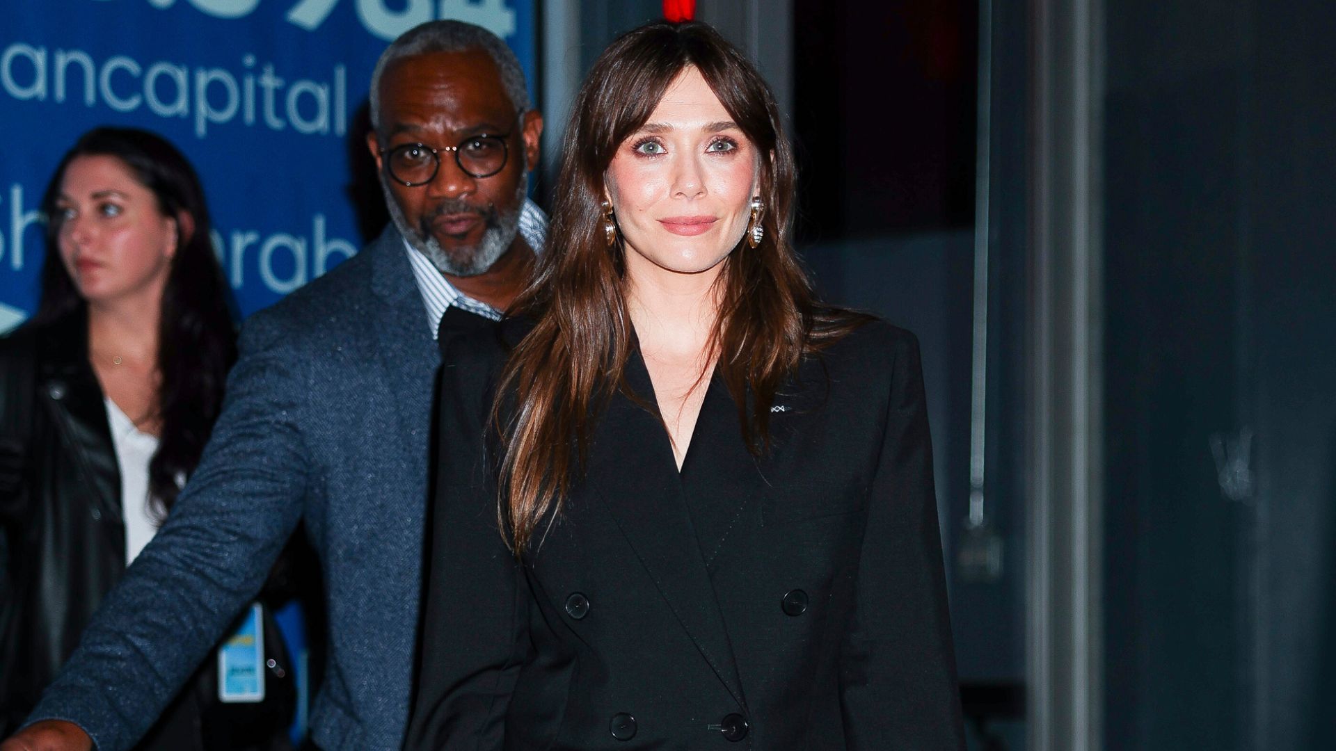 Elizabeth Olsen wears bow heels with a black double breasted blazer and a black skirt.