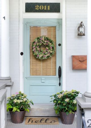 A cottage-style front porch with pot plants, a pale blue door and gold mailbox.