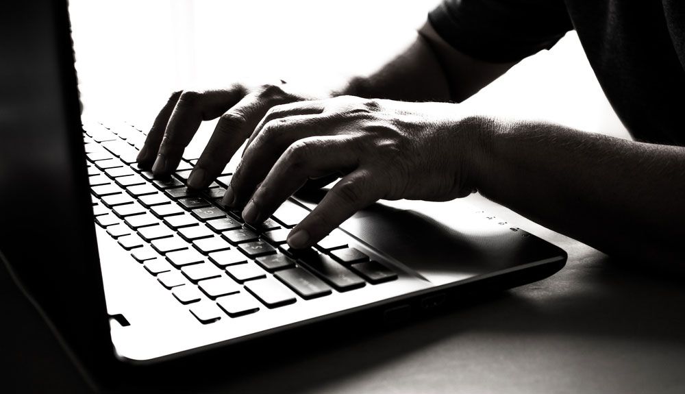 Hands type on a laptop keyboard.