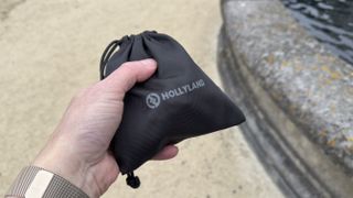 A hand holds a Hollyland branded drawstring bag containing the Lark M2S and its accessories