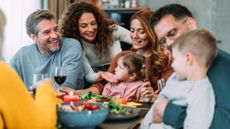 Photo of happy multi-generation family and friends, including several children, gathering for a meal around a dinner table