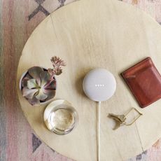 smart home ecosystem Google Nest Mini on a wooden coffee table beside a plant pot and a wallet