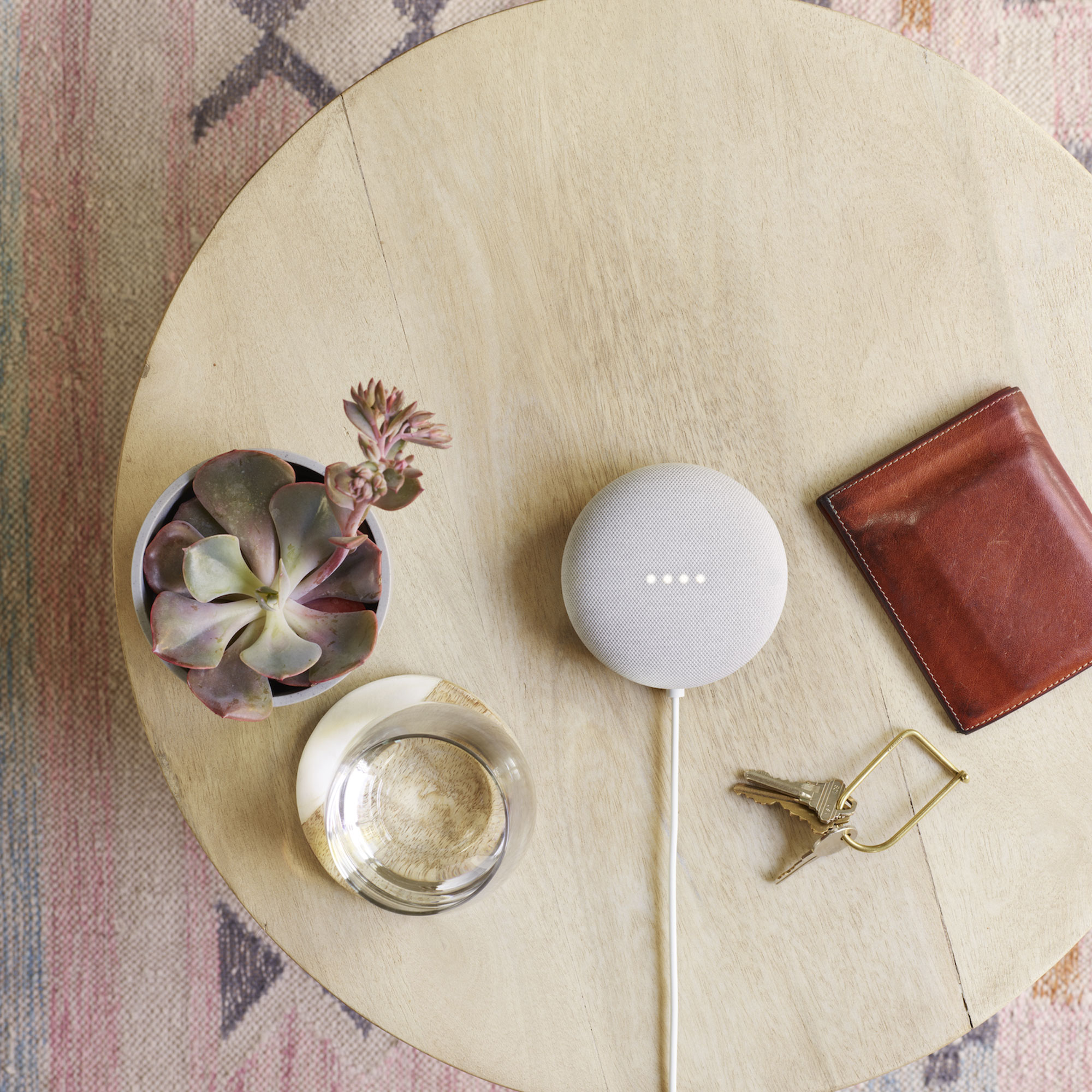Google Nest Mini on a wooden coffee table beside a plant pot and a wallet