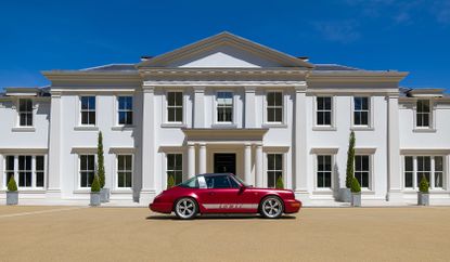 A red porsche car is parked outside a large white house