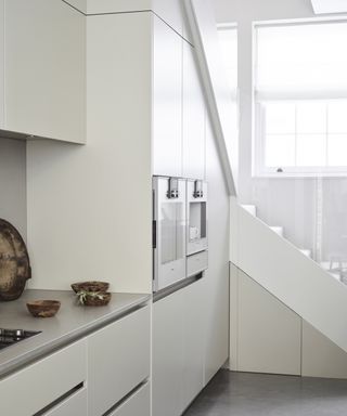 A modern kitchen with double height white cabinets, and ones that fit in with the staircase