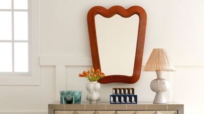 Curvy mirror above a siaboard with a lamp and small trinket decor