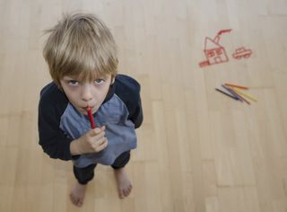 child looking up after drawing a house on wood floor with crayons
