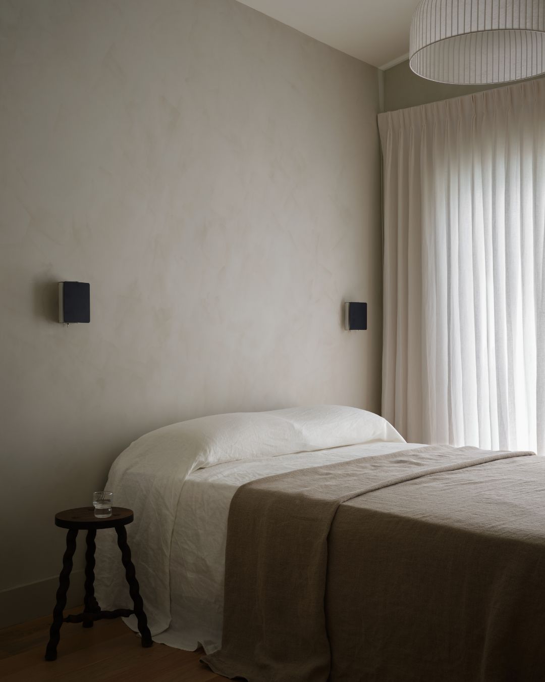 A small bedroom with gray, limewash walls, and a white and brown bedding, with a single bed placed in the corner
