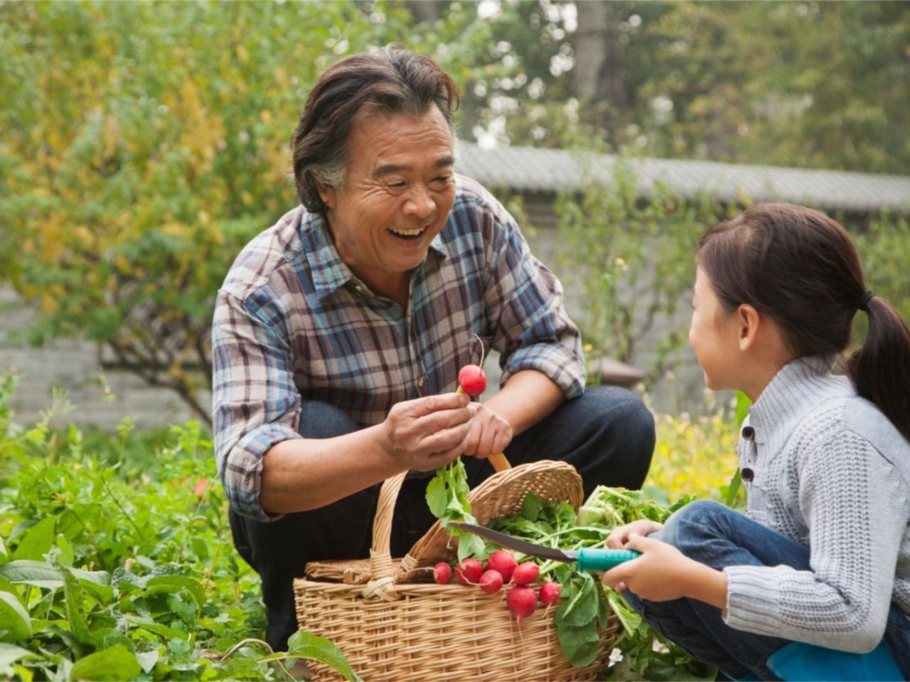 A smiling older man holds up a radish to a young girl