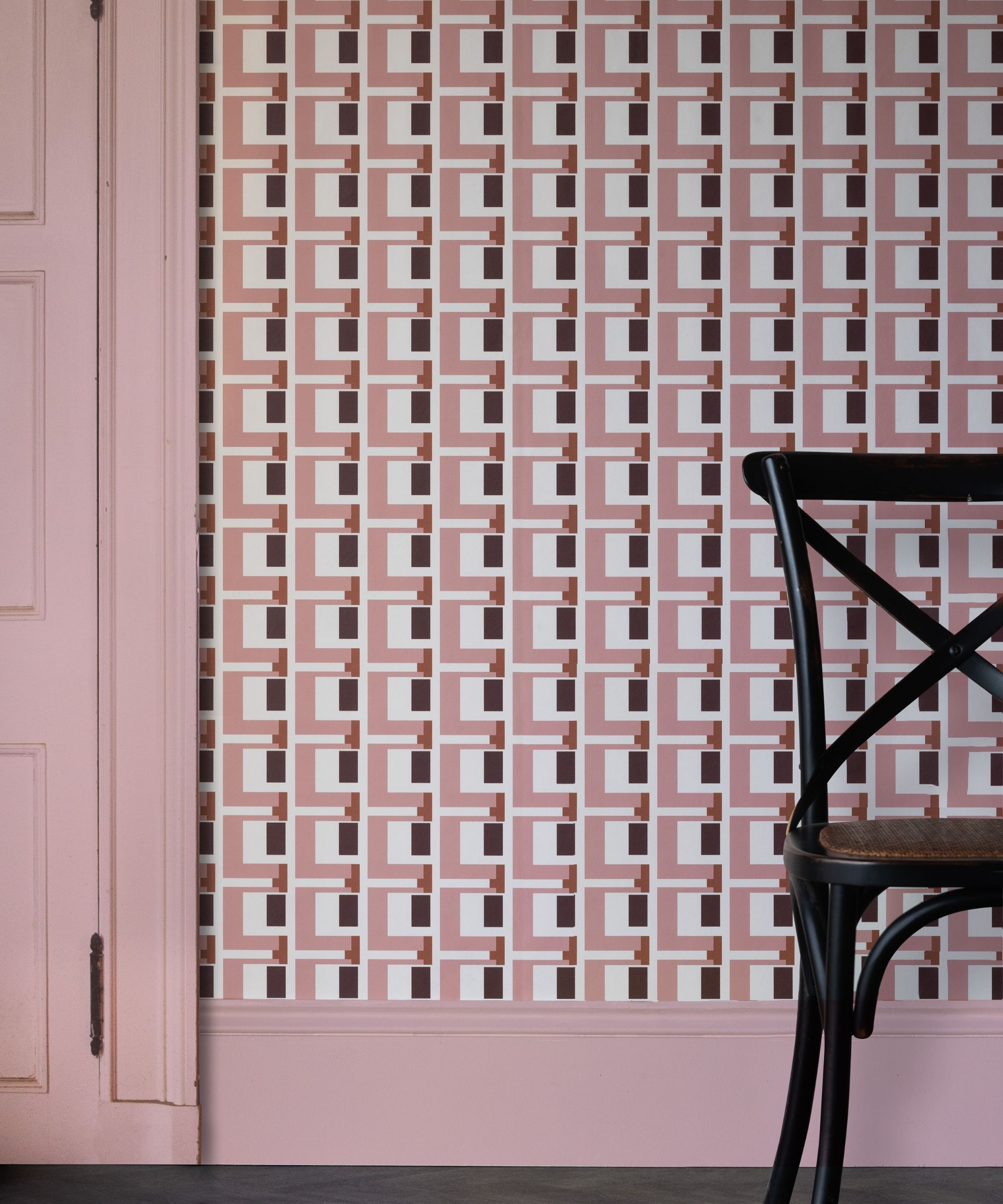 Pink geometric wallpaper with square patterns behind a black wooden chair and pale pink door.