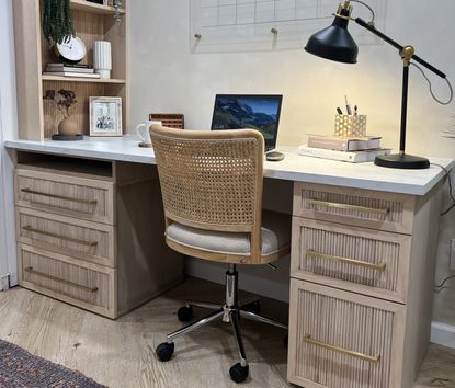 A home office with a fluted desk with a marble top and a rattan chair