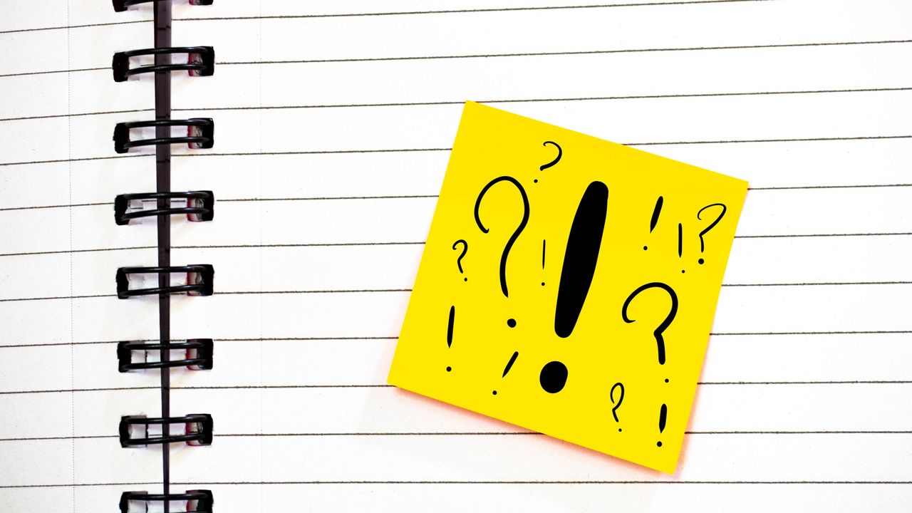 A notebook with a yellow Post-It Note bearing multiple question marks and a big exclamation point.