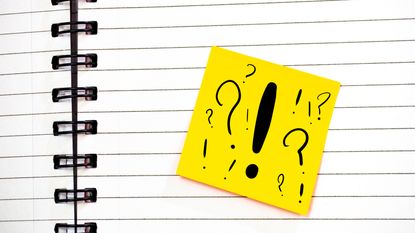 A notebook with a yellow Post-It Note bearing multiple question marks and a big exclamation point.