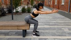 Woman exercises outside, squatting back on to the edge of a bench