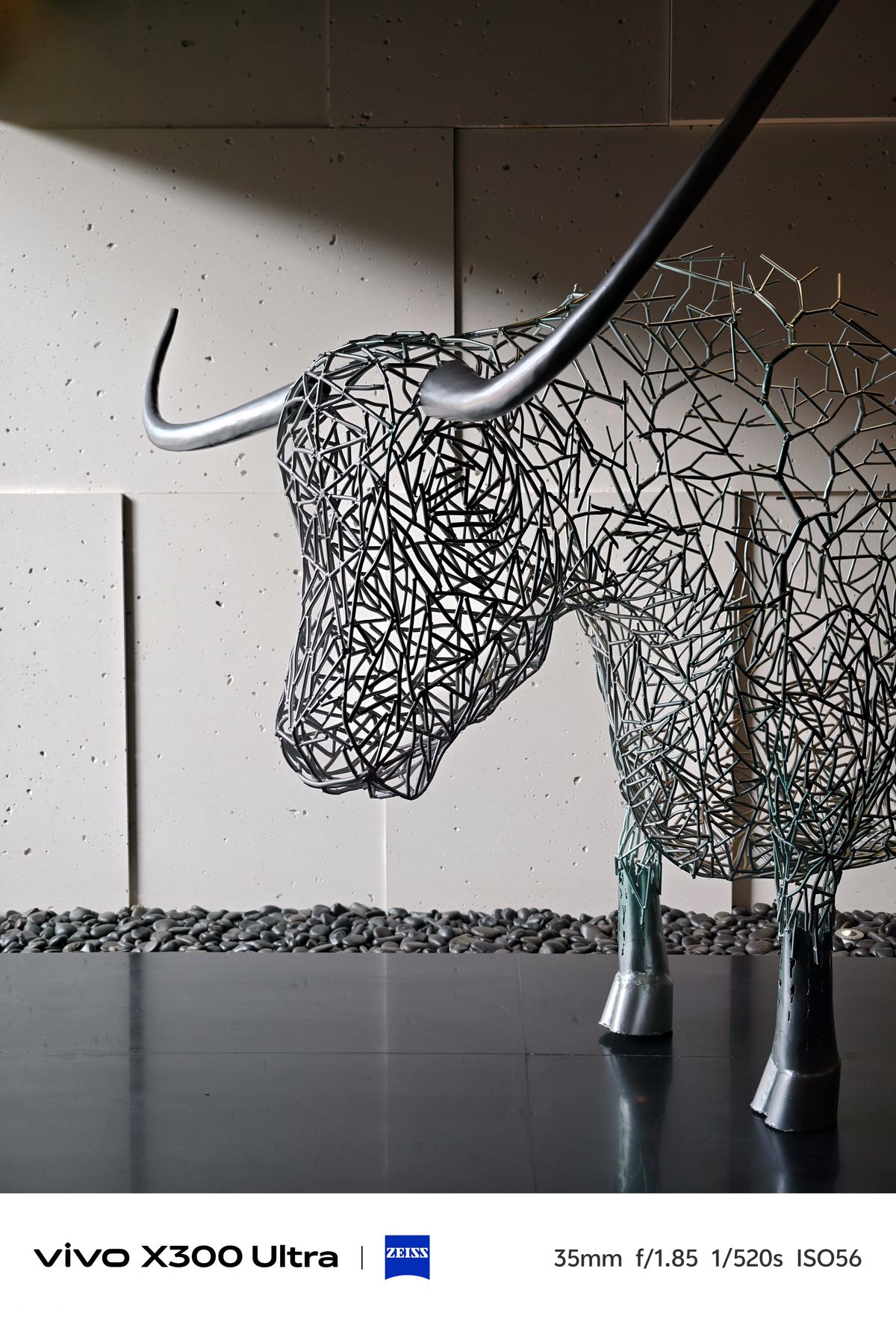 A modern indoor sculpture of a horned bull crafted entirely from interconnected grey metal wires.