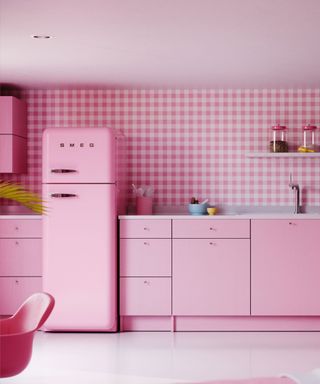 A bubblegum pink kitchen with a Smeg fridge, pink cabinets, a pink checkered wall with shelves on it, and a pink concrete floor