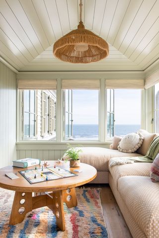 Pale geen room overlooking the sea with colourful rug with pink polka dot sofa, wooden table and color matched woven lampshade