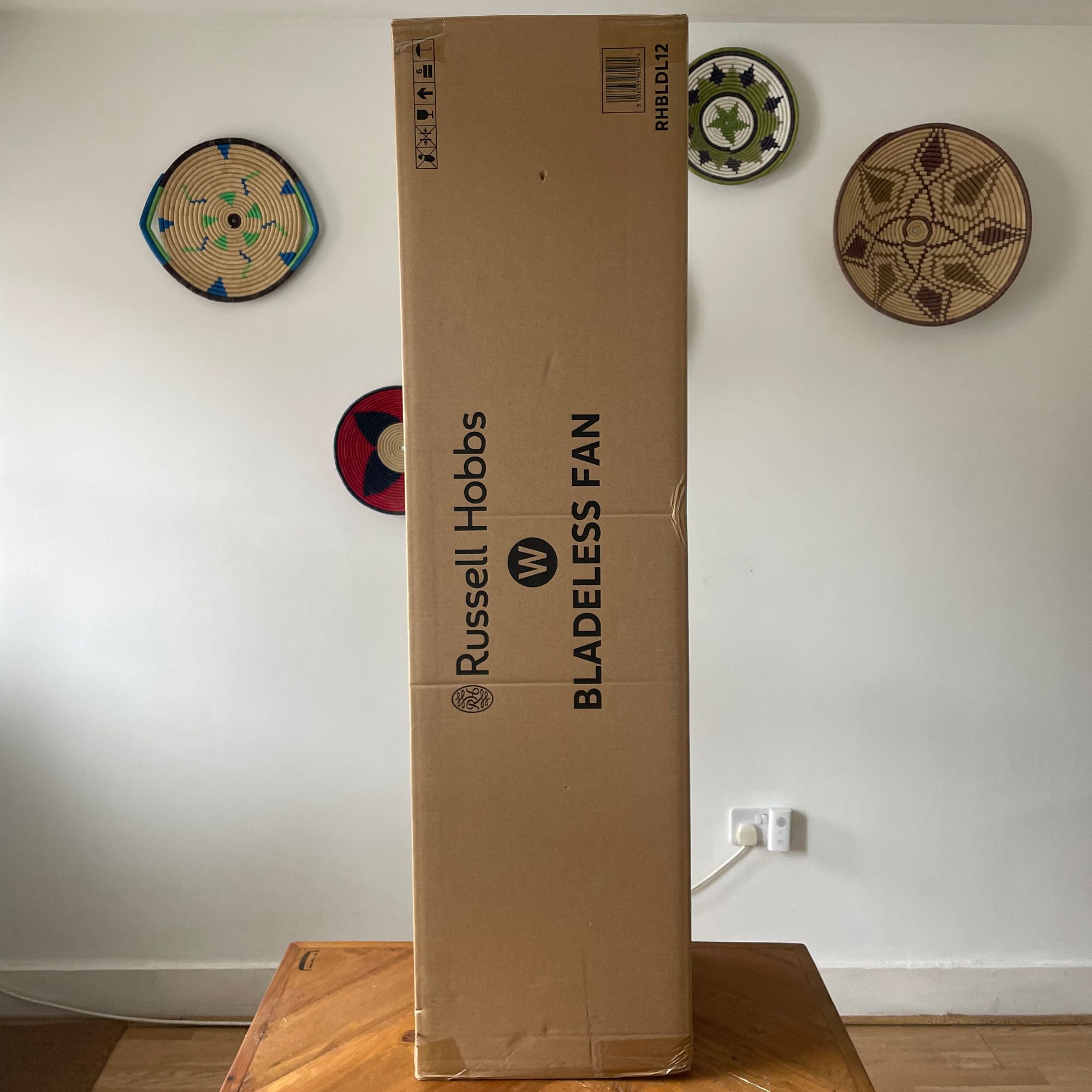 Box of the Russell Hobbs RHBLDL12 Bladeless Tower Fan sitting on a wooden table in front of a white wall