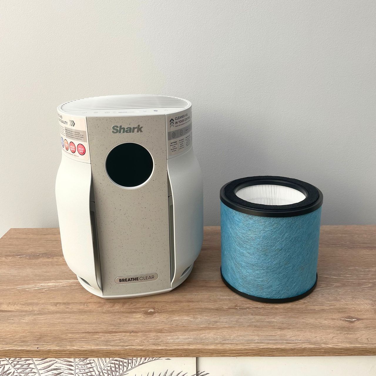 Shark BreatheClear Compact Air Purifier with NeverChange6 and its filter sitting on a wooden unit in front of a grey wall