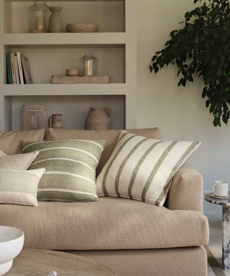 A beige boucle sofa with cream and green striped thro pillows in a neutral living room.