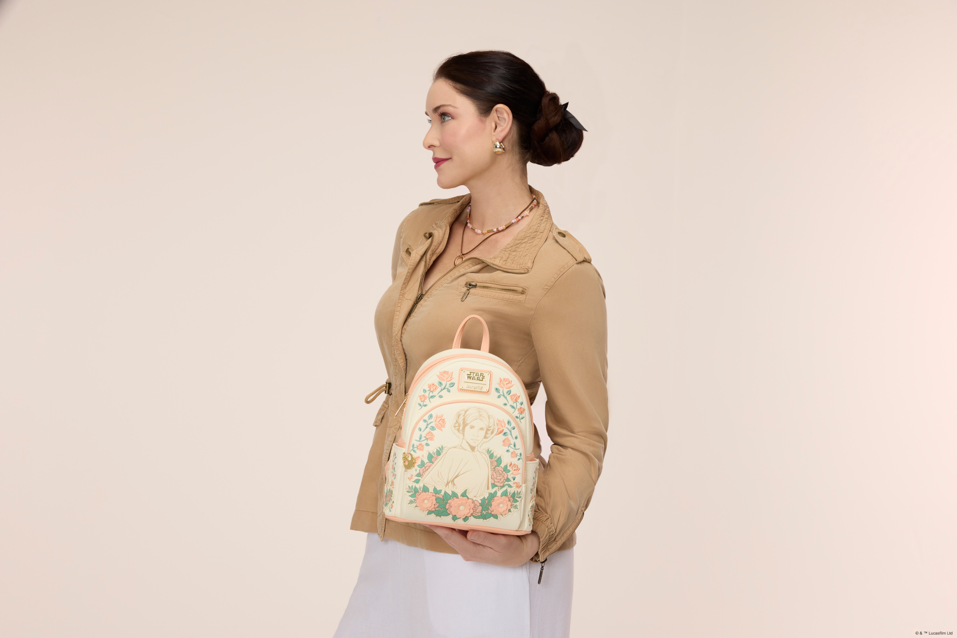 A woman holds up a Loungefly Mini Backpack with Leia on the front, while standing in a pink background