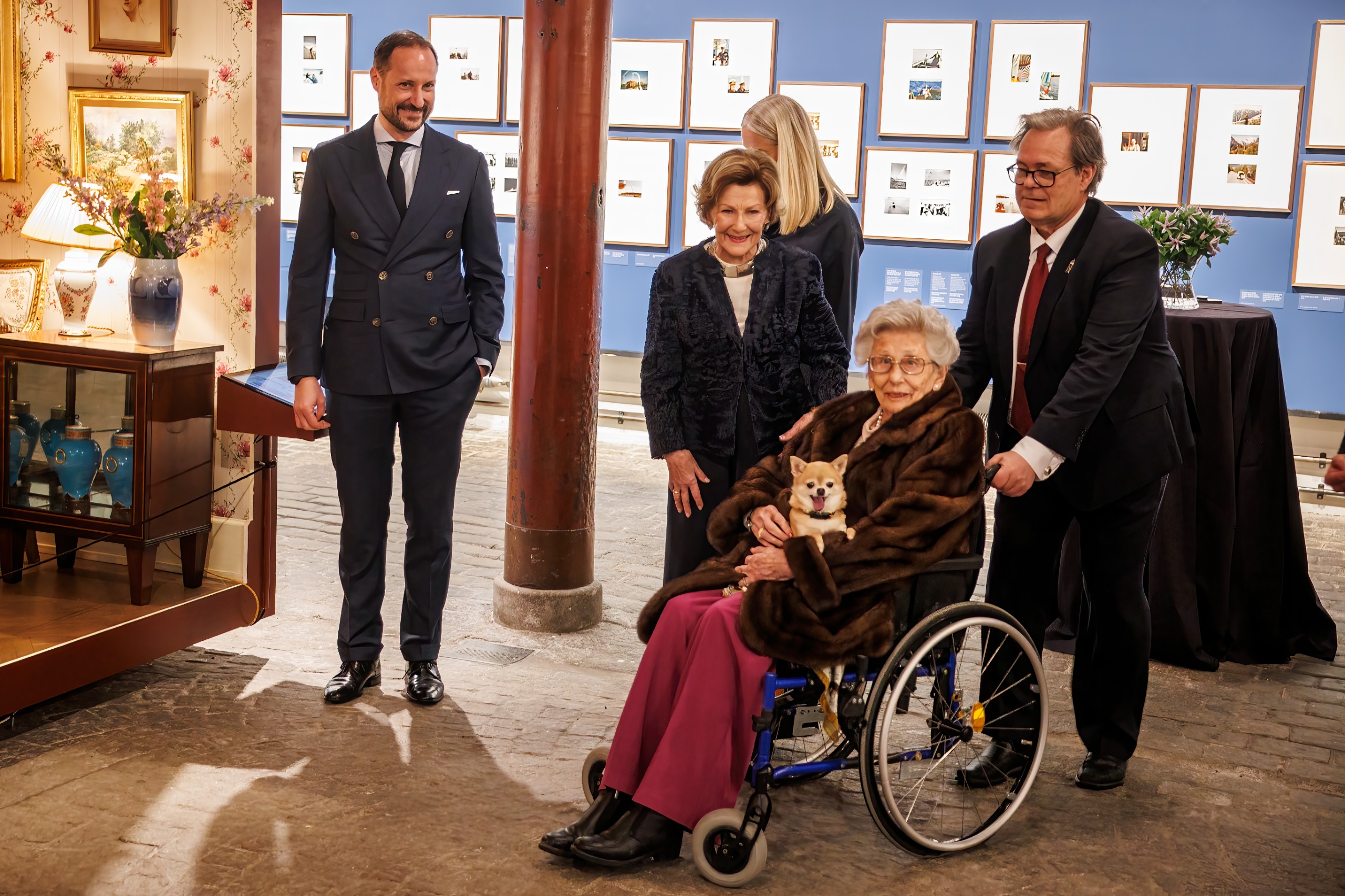 King Haakon, King Sonja and Princess Astrid sitting in a wheelchair holding her dog