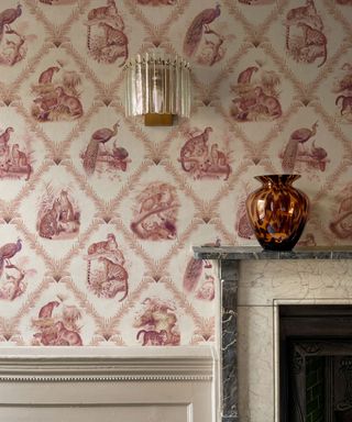 Close up of pink wallpaper featuring a jungle style print of animals, marble fireplace, wall light, vase on mantel