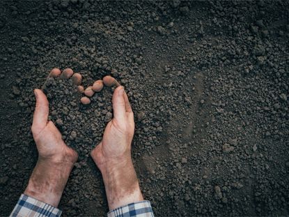 A man's hands lift soil from the ground in a heart shape