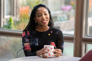 Jessica Williams as Gaby, sitting at a table and holding a mug with a flower handle, in 'Shrinking'