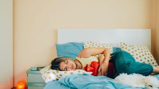 woman laying on her bed holding a hot water bottle to her stomach