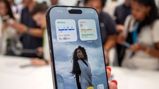 iPhone 16 Plus smartphone held in hand showing woman on screen, crowd in background