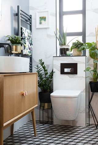 Retro vanity unit, graphic geo floor tiles, wall mounted toilet, and plenty of houseplants in stylish bathroom scheme.