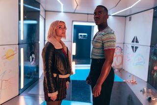 Ruby (Millie Gibson) and the Doctor (Ncuti Gatwa) stand in a corridor in a space station, looking around at their surroundings. There are drawings in crayon on the walls, apparently drawn by small children.