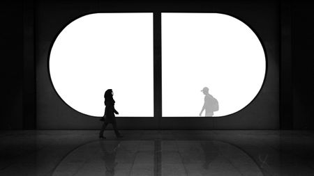 Silhouettes of two people walking opposite each other, separated by a large circular window