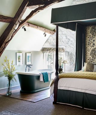 bedroom with four poster bed with William Morris fabric and dark blue freestanding tub in 12th century Cotswolds country house