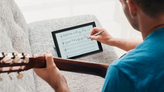 Man holding guitar writing sheet music on electronic tablet