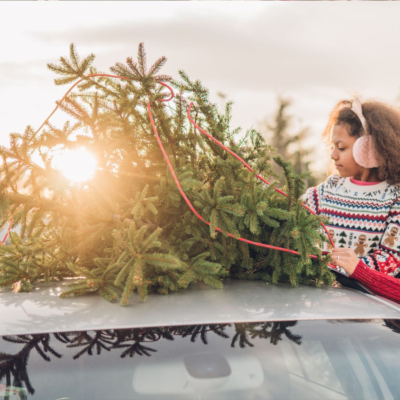Christmas tree tied to a car roof by happy couple and their daughter