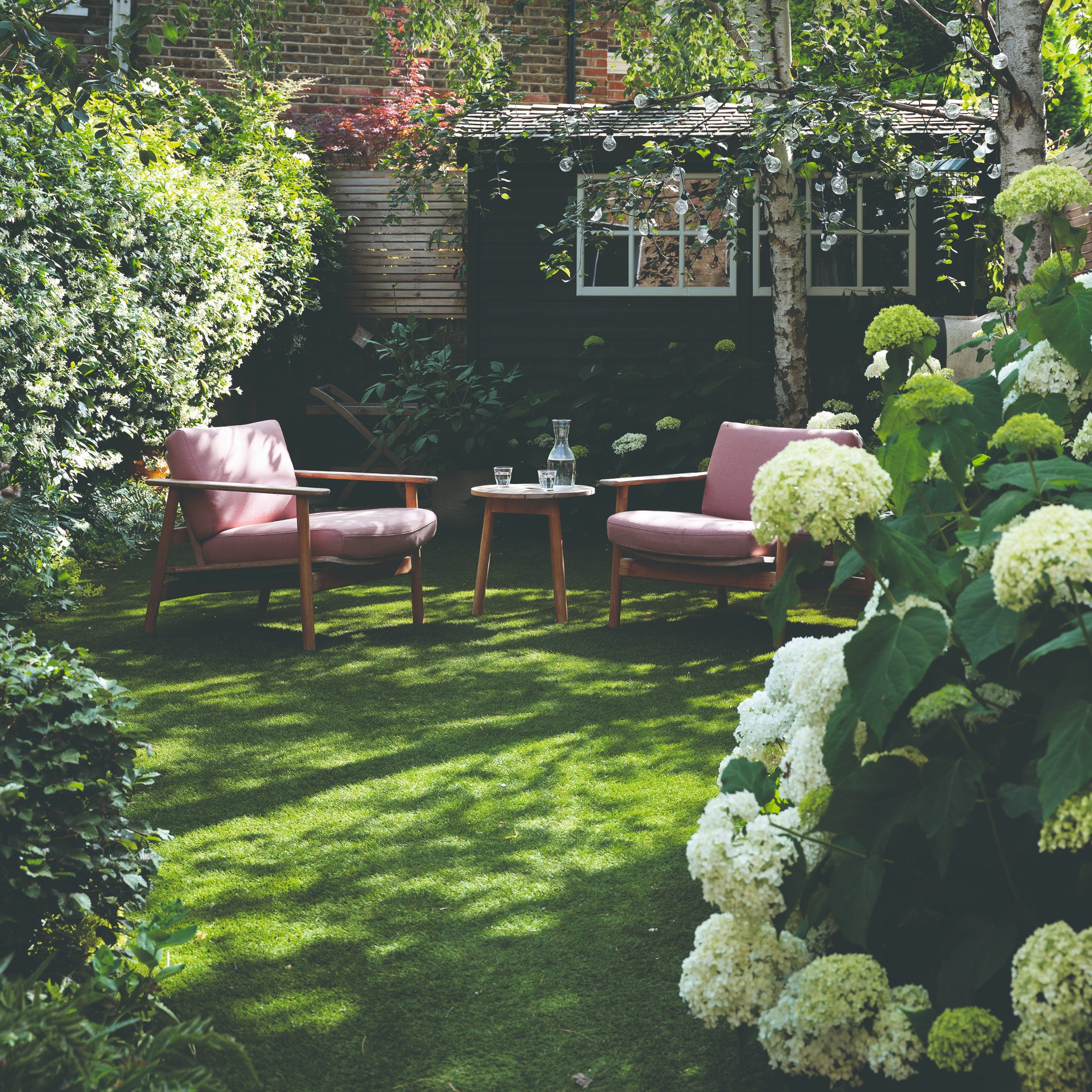 A garden with a seating set and a bush of hydrangeas