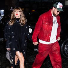 Taylor Swift in a long, crystal-embellished black coat and Travis Kelce, wearing red pants and a matching red jacket, while out in New York City on December 28, 2024