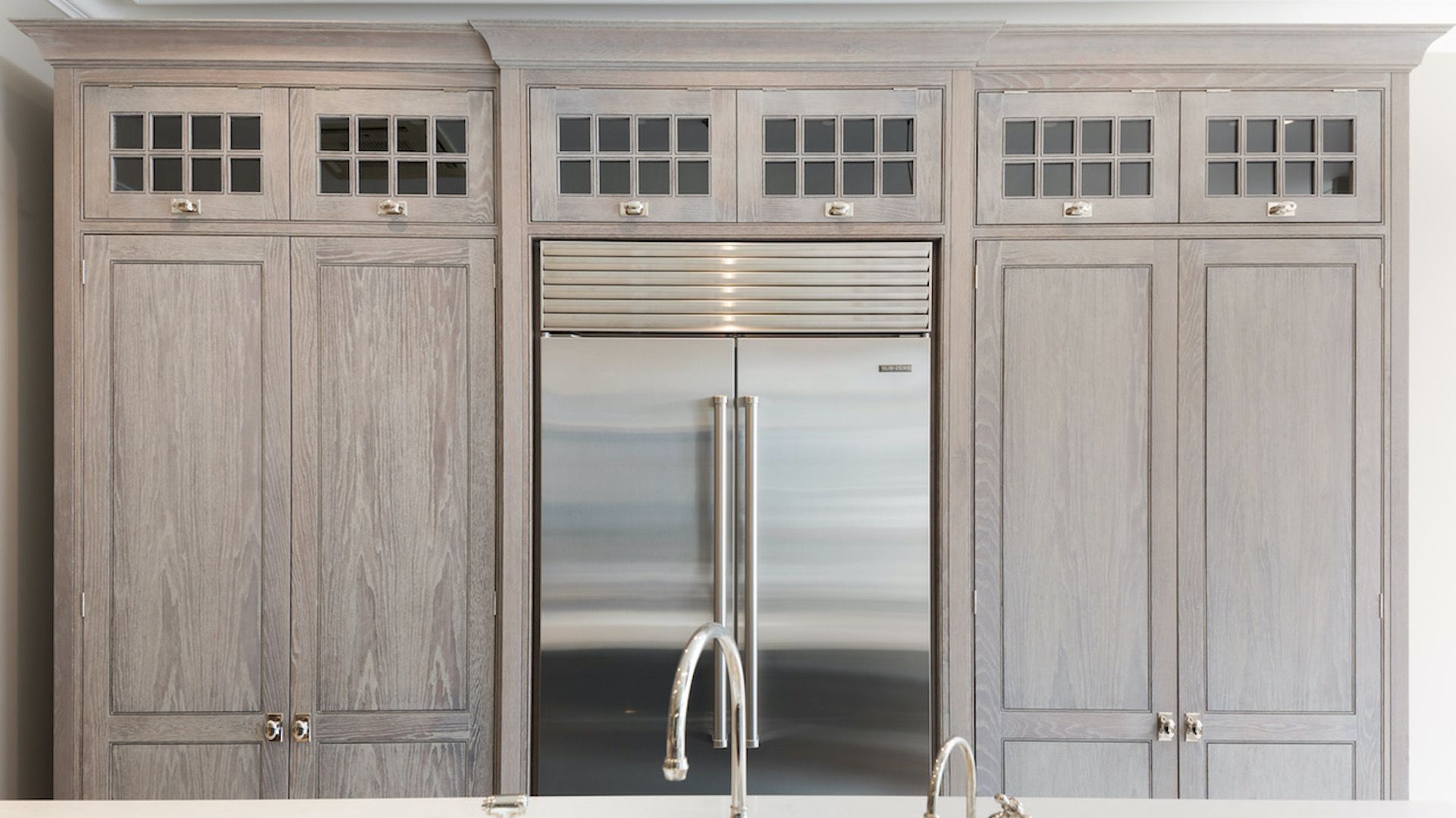 Limed wood kitchen cabinets floor-to-ceiling with stainless steel fridge placed in the middle to break up the small kitchen storage idea