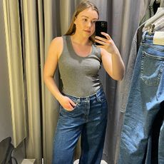 Woman in dressing room wears grey vest and blue jeans