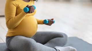 Pregnant woman exercises on the floor with light dumbbells