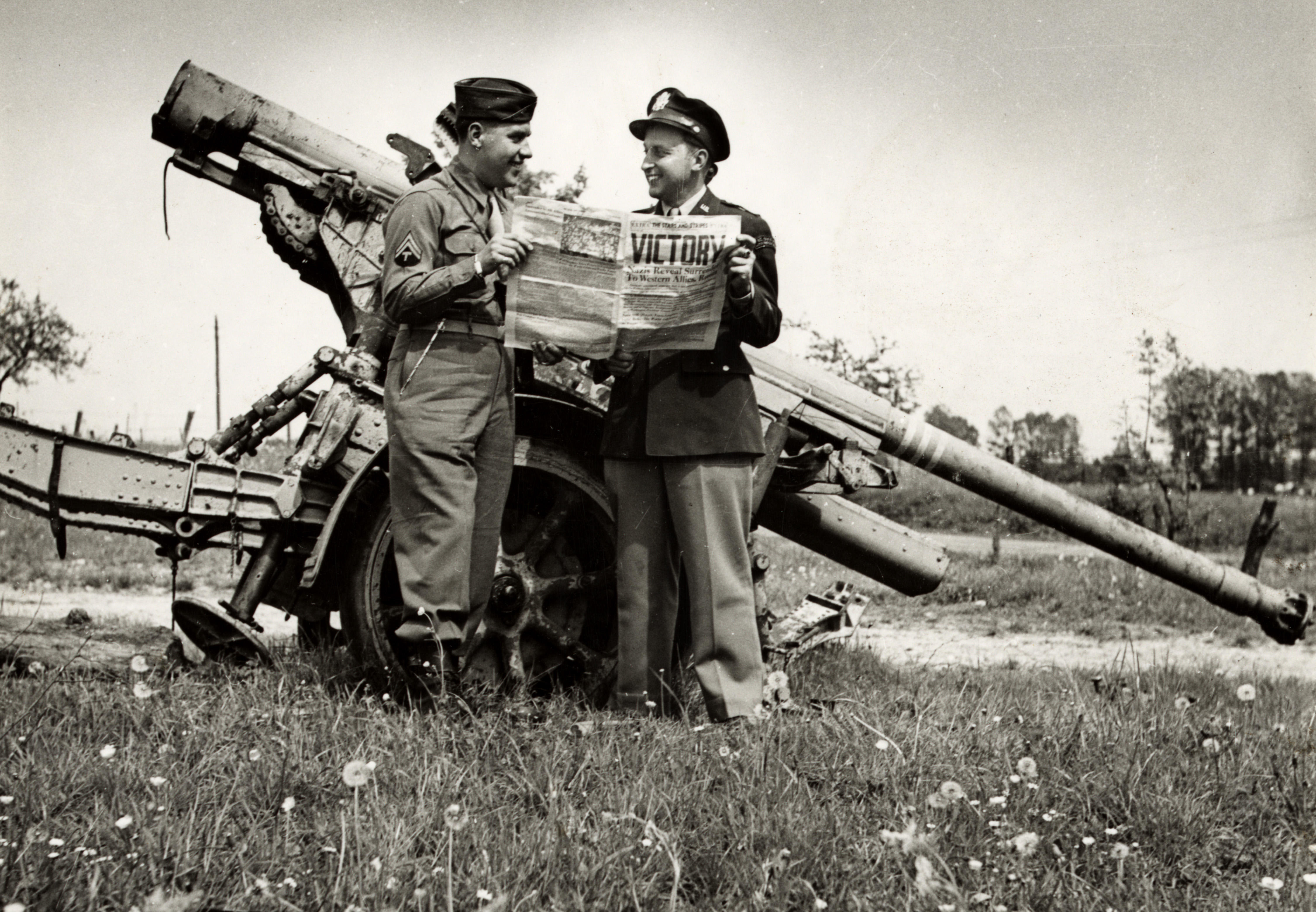 Soldiers read of victory, standing by a German 88mm gun at Verdun, France on VE Day