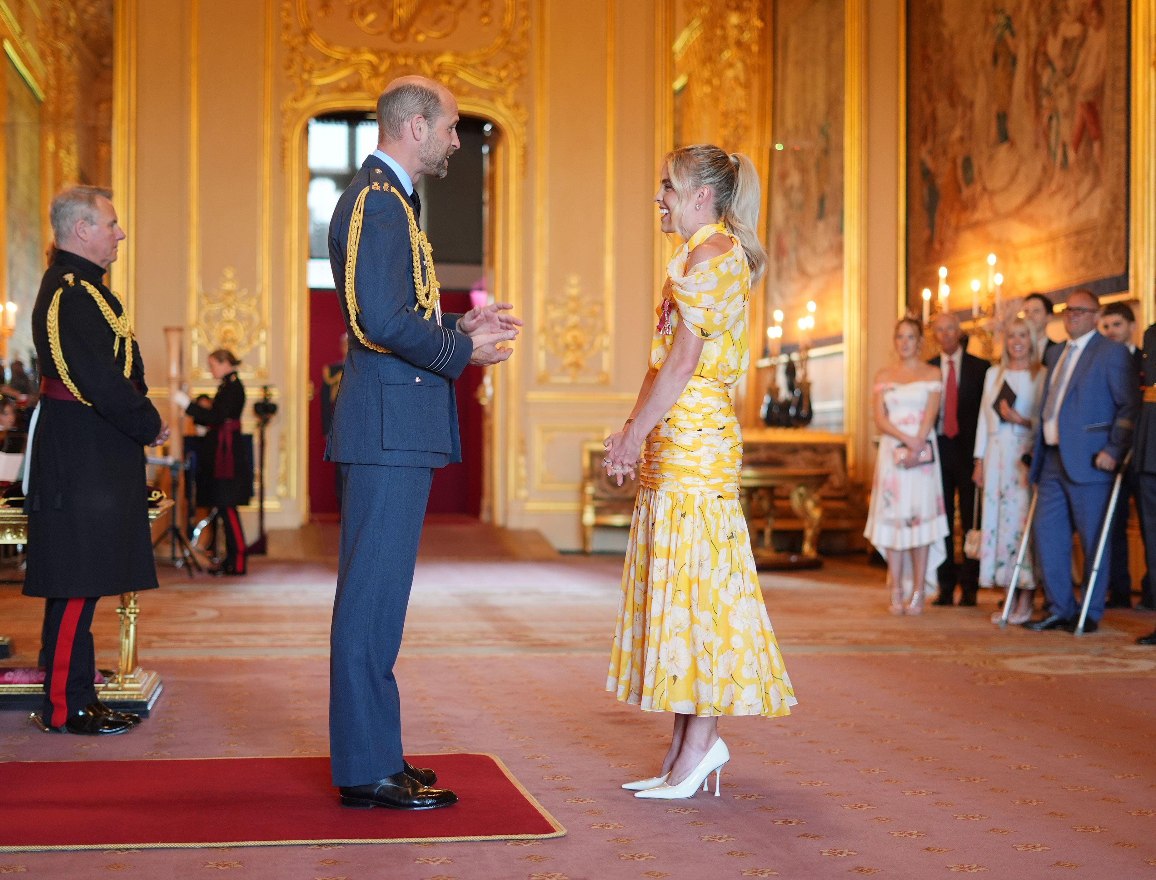 Prince William speaking to athlete Keely Hodgkinson, wearing a yellow dress, at Windsor Castle investiture