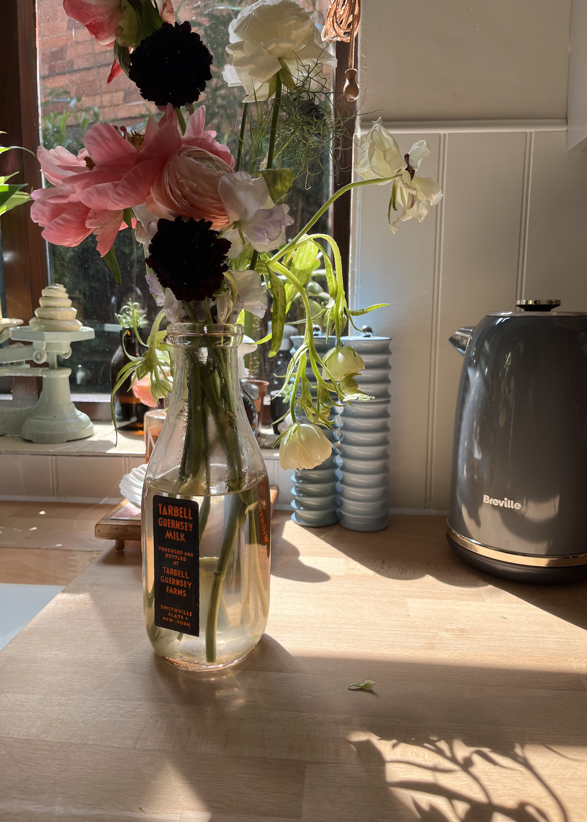 A vase of flowers on a wooden kitchen countertop with a white tongue and groove panelled backsplash